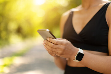 Closeup of African American womans hands holding smartphone during workout outdoors. Fitness tracking, lifestyle technology and modern active living