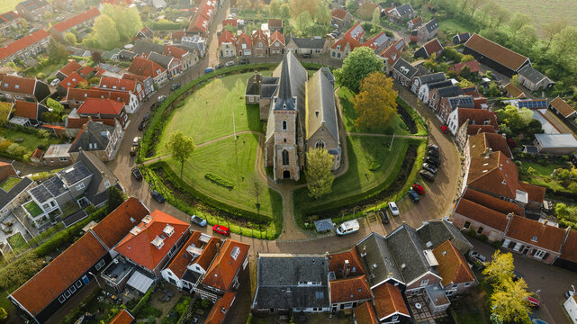 Aerial view of the Radboud Church standing majestically within its circular moat, the red roofs of surrounding houses adding warmth to the serene Dutch landscape, Garnwerd, Netherlands.