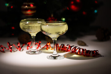 Two elegant glasses filled with sparkling beverages sit on a table, decorated with bright ribbons and holiday ornaments in the background, evoking a celebratory atmosphere during a festive gathering.