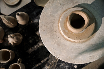 A top-down view of a pottery wheel with a clay vessel in the center, surrounded by other clay pottery items.