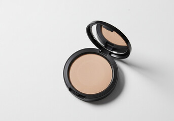 Close-up shot of a round, open compact powder with a mirror, on a white surface.