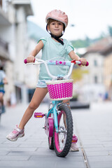 Cute girl wearing cycling helmet and riding bike at park. Portrait of a playful funny girl in a pink safety helmet on her bike
