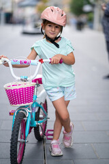Cute girl wearing cycling helmet and riding bike at park. Portrait of a playful funny girl in a pink safety helmet on her bike