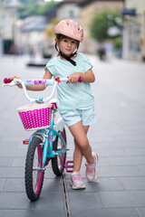 Cute girl wearing cycling helmet and riding bike at park. Portrait of a playful funny girl in a pink safety helmet on her bike