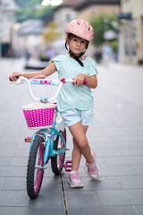 Cute girl wearing cycling helmet and riding bike at park. Portrait of a playful funny girl in a pink safety helmet on her bike