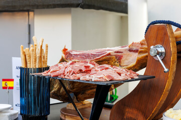 Whole Iberian ham shoulder and slices with breadsticks arranged on a buffet table