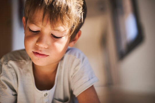 Close up of boy indoors looking down with concentration, child focused and thoughtful in natural light - Powered by Adobe