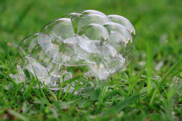 Photographed from close range, soap bubbles are piled up on green grass with a blurred background of green grass