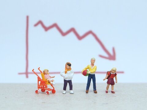 Mini toy of action figure at table with blurred background. Miniature photography concept design. Minifigure of father, baby at stroller and mother character with down arrow chart.