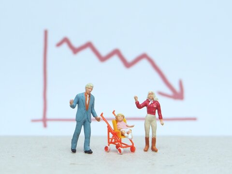 Mini toy of action figure at table with blurred background. Miniature photography concept design. Minifigure of father, baby at stroller and mother character with down arrow chart.