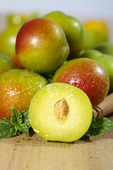 Fresh Red and Green Plums Half Cut Showcase on Wooden Board with Mint