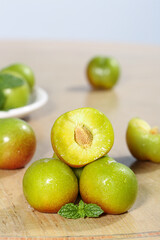 Fresh Green Plums Cut Into Pieces Showing Yellow Flesh on Wooden Board