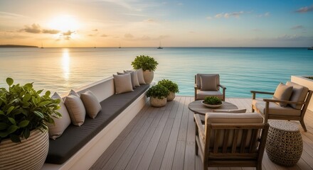 An elegant oceanfront patio at sunset featuring a cushioned bench lounge chairs and potted plants overlooking calm turquoise waters with distant sailboats