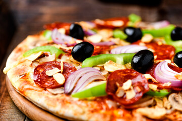 Pizza with chorizo ​​sausage, mozzarella cheese, green pepper and black olives. Rustic wooden background. Soft focus.	