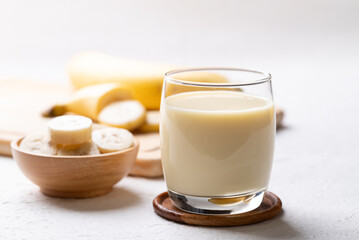 Banana milk in glass with sliced banana and fruit on white background