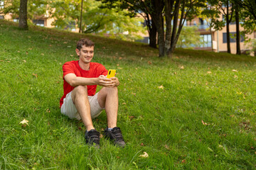 Young man using smartphone sitting on grass in park