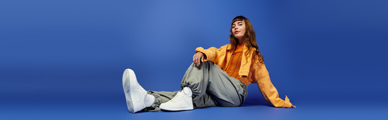 Fashionable young woman poses stylishly against a vibrant blue backdrop with a confident attitude