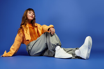 Young stylish woman showcases trendy street fashion against vibrant blue backdrop © Bliss