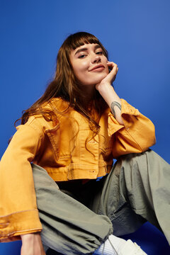 Stylish young woman in vibrant attire poses against a striking blue backdrop with confidence