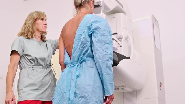 50-year-old woman undergoes mammography procedure on special medical equipment mammograph with the help of assistant in modern clinic. Regular medical examination, screening for breast cancer