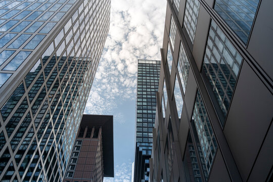 Upward perspective of Frankfurt skyscrapers against cloudy sky, vertical composition capturing ambition, architectural rhythm and power of European financial core