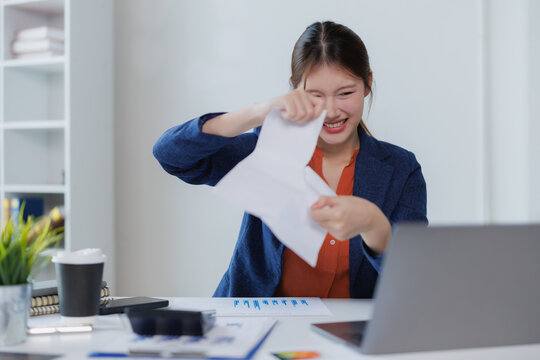 Young businesswoman is tearing a document apart at her office desk, celebrating achieving a goal or completing a challenging project, expressing joy and relief in her professional environment