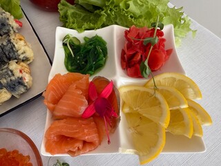 Red fish caviar swirls on the table with lemon, eco and natural dietary food. lemon wasabi ginger seaweed chuka red fish white table decorated with flowers and microgreens