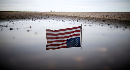 American flag floats in shallow water on a desolate beach, reflecting patriotism and somber remembrance on a cloudy day.