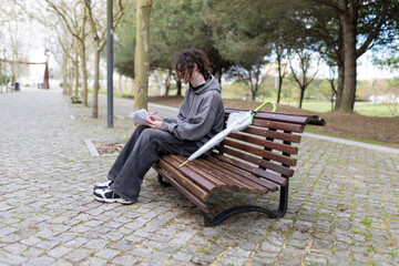 Fototapeta premium Young man writing on a bench in the park with umbrella
