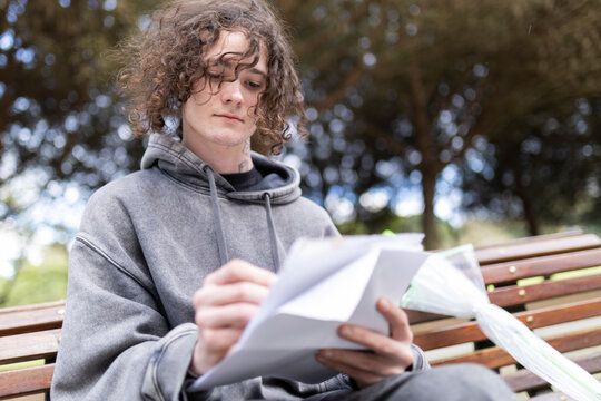 Young man reading documents on park bench - Powered by Adobe