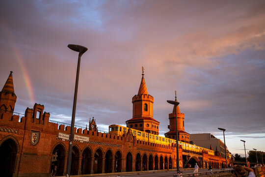 Panoramic view of Oberbaum Bridge in Berlin with rainbow at sunset, historic red brick arches and towers representing cultural heritage and iconic German landmark