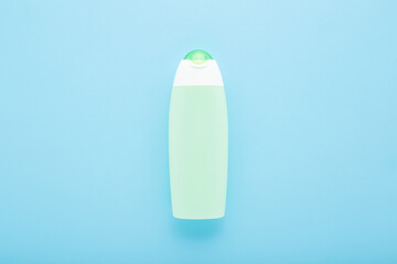 Green plastic shampoo or shower gel bottle on light blue table background. Pastel color. Care about clean and soft body skin. Beauty product. Closeup. Top down view.