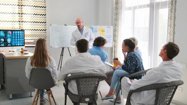 Doctor in white coat presents new medical formula on board during hospital seminar. Healthcare staff raise hands, ask questions and debate, engaging in professional training and discussion.