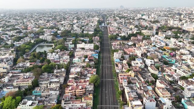 Aerial video of Chennai, India, showing vast urban sprawl. A long stretch of railway tracks cuts through the dense cityscape, with a serene temple tank and lush greenery providing a peaceful contrast.