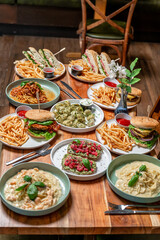 Diverse dishes at a vibrant eatery. Delicious meals including burgers, pasta, and snacks are spread across a wooden table in a cozy dining atmosphere.