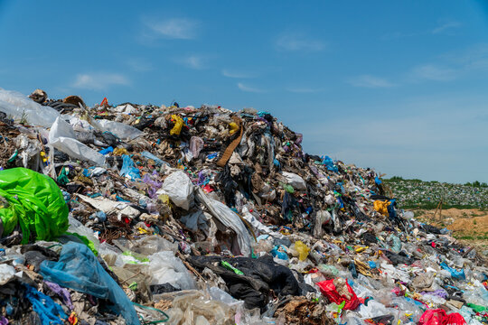 Massive heap of plastic waste and garbage at an open outdoor landfill site under a clear blue sky.