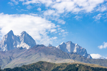 Rocky mountains partially covered by green vegetation under a blue sky with clouds in Georgia