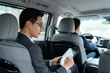 A businessman is using a tablet inside a vehicle, likely engaged in work-related activities during a commute.