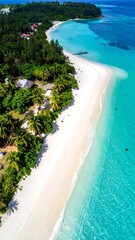 Fototapeta premium High-angle view of a pristine white-sand beach fringed by lush tropical vegetation, turquoise waters, and a tranquil atmosphere.