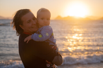 Mother holding her child on sunet. Sea view.