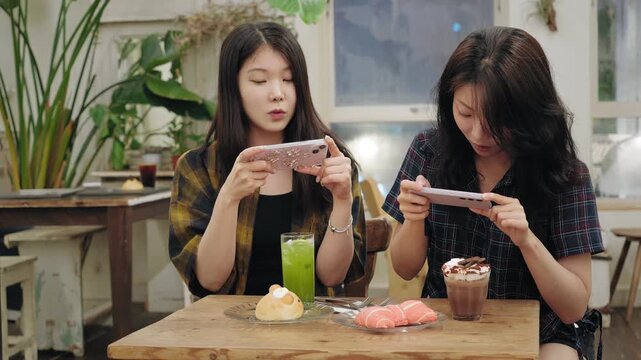 Two Asian Korean girl friends taking photos of their food and drinks in a cafe sharing content on social media