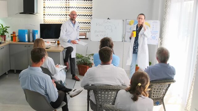 Bald pharmaceutical company representative and chief doctor in lab coat debate new product during hospital seminar. Active discussion with medical staff about drug properties and innovations.