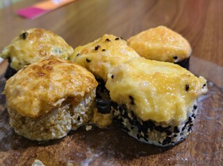 Delicious baked sushi rolls with creamy toppings on a wooden serving board closeup