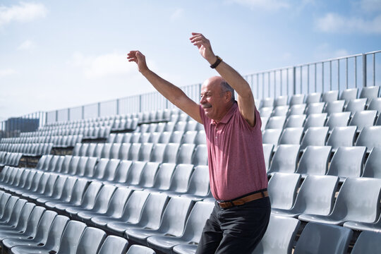 elderly man sitting alone at stadium cheering for his team, celebrating a goal