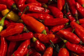 A pile of fresh birds eye red chili peppers with green stems, captured in close up