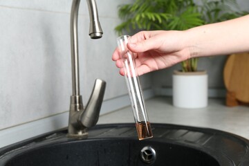 Woman taking sample of water from faucet indoors, closeup. Quality testing