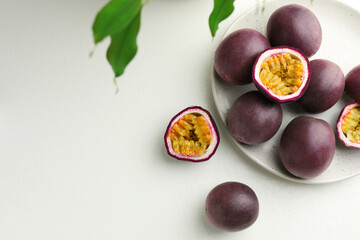 Fresh passion fruits with green leaves on white table, flat lay. Space for text
