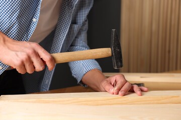 Man hammering nail into wooden plank indoors, closeup