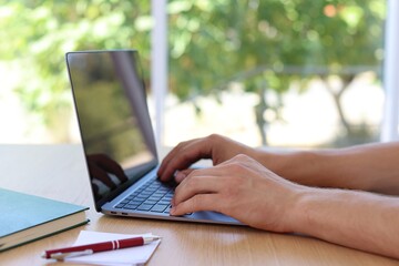 Man working on laptop at wooden table indoors, closeup