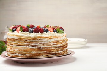 Delicious crepe cake with fresh berries on white wooden table, closeup. Space for text
